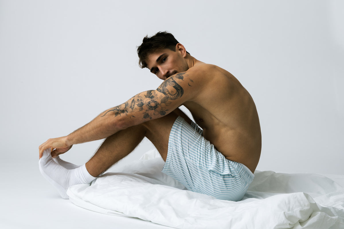 Mężczyzna w niebieskich szortach do spania w paski z TENCEL™ Modalu, otulony białą kołdrą – Club Harbour